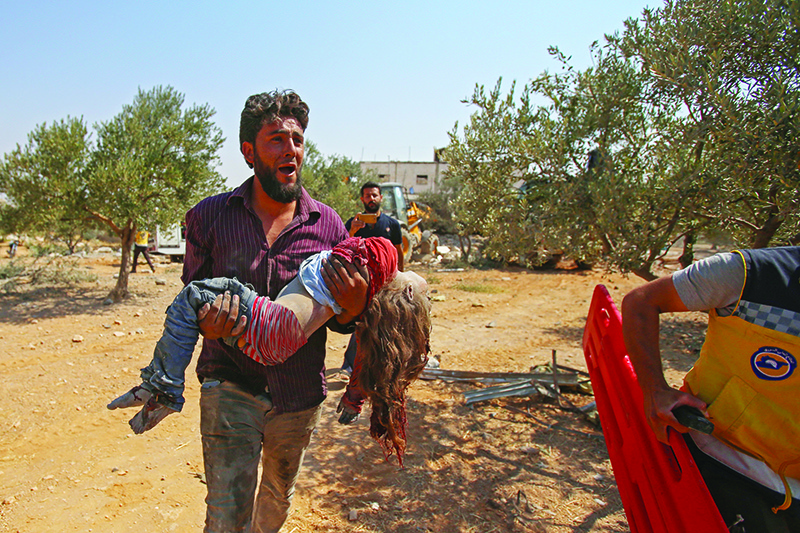 TOPSHOT - EDITORS NOTE: Graphic content / A Syrian carries the body of a child at the site of a reported regime air strike on the village of Deir Sharqi on the eastern outskirts of Maaret al-Numan in Syria's northern province of Idlib on August 17, 2019. - Regime air strikes killed one woman and six of her children in northwest Syria, a war monitor said, a day after Russian bombardment pummelled a nearby displacement camp. (Photo by Abdulaziz KETAZ / AFP)