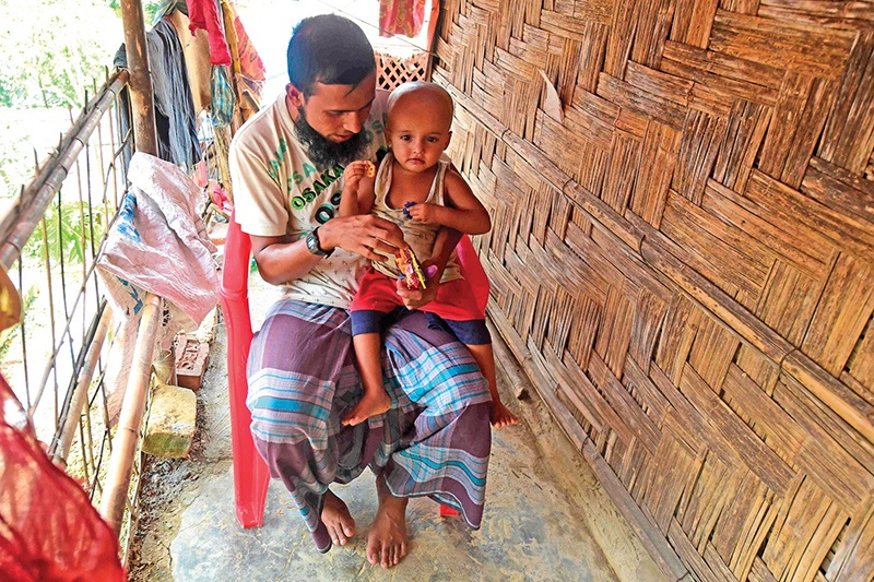 Rohingya refugee Mohammad Selim interacts with his son Ahmad Shah, who was born two years ago when a brutal military clampdown eventually drove away some 740,000 Rohingyas to Bangladesh, at Balukhali refugee camp near Cox's Bazar on August 25, 2019. - Heavily pregnant Rohingya mother Rashida Khatun fled her home in a remote Rakhine village two years ago, bone-tired but desperate to find a safe place to give birth to her baby. Walking for hours with her husband and three children, Khatun then took a treacherous sea journey in inclement weather to reach Shah Porir Dwip at the southeastern tip of Bangladesh. (Photo by MUNIR UZ ZAMAN / AFP) / To with 'BANGLADESH-MYANMAR-REFUGEE-CHILDREN-ROHINGYA'
