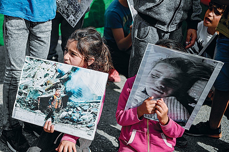 RITSONA: Children hold photographs, as Syrian Kurd refugees protest at the Ritsona camp, yesterday after Turkey launched an assault on Kurdish forces in northern Syria with air strikes and explosions reported along the border. —AFP