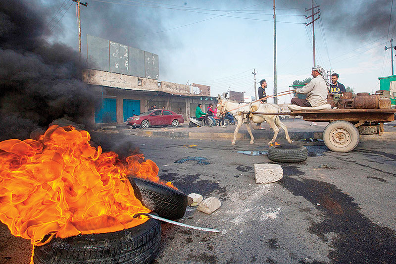 BASRA: A man rides his donkey-drawn carriage past burning tyres during a demonstration in this southern city yesterday. - AFP  