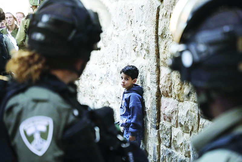 Israeli soldiers look at a Palestinian boy as he waits by the wall for Israeli settlers touring the old city and market of Hebron in the occupied West Bank to pass, on December 21, 2019. (Photo by HAZEM BADER / AFP)