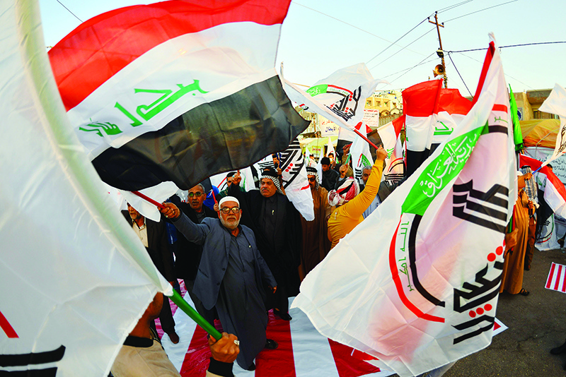 Iraqis wave Hashed Al-shaabi armed network flags on December 30, 2019, during a demonstration to denounce the previous night's attacks by US planes on several bases belonging to the Hezbollah brigades near Al-Qaim, an Iraqi district bordering Syria. - US air strikes against a pro-Iran group in Iraq reportedly killed at least 25 fighters, triggering anger in a country caught up in mounting tensions between Tehran and Washington. (Photo by Haidar HAMDANI / AFP)