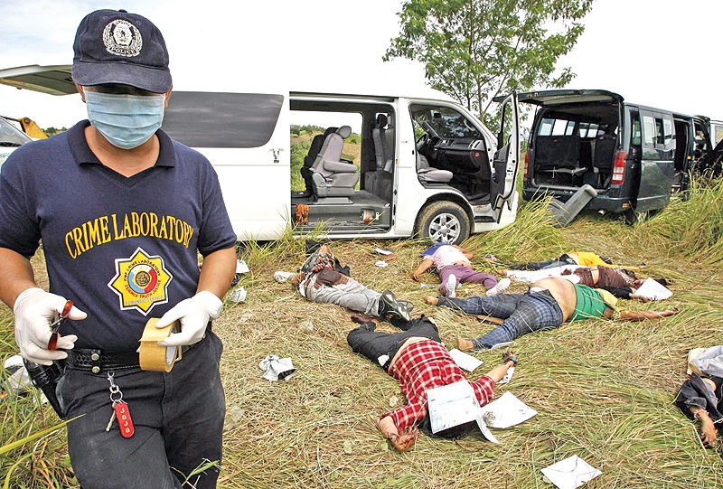 This file photo taken on November 24, 2009 shows a police investigator gathering evidence next to bodies of victims after gunmen shot a group of people including media workers in Ampatuan town, Maguindanao province. — AFP
