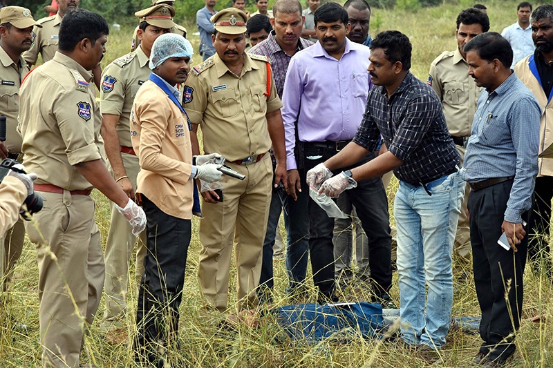SHADNAGAR, India: A forensic official holds a gun as police officers gather around the body of man at the site where police officers shot dead four detained gang-rape and murder suspects on Friday. - AFP