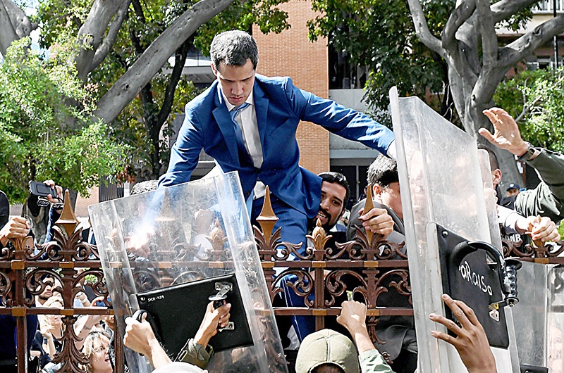 Venezuelan opposition leader and self-proclaimed acting president Juan Guaido is helped to climb a railing in an attempt to reach the National Assembly building in Caracas, on January 5, 2020. - Venezuela's opposition lawmaker Luis Parra -a rival to Juan Guaido- declared himself parliament speaker, as Guaido and fellow opposition lawmakers were blocked from entering the National Assembly. Guaido had been expected to be re-elected parliament speaker but only regime lawmakers and opposition deputies critical of Guaido were allowed to enter the building. (Photo by Federico Parra / AFP)