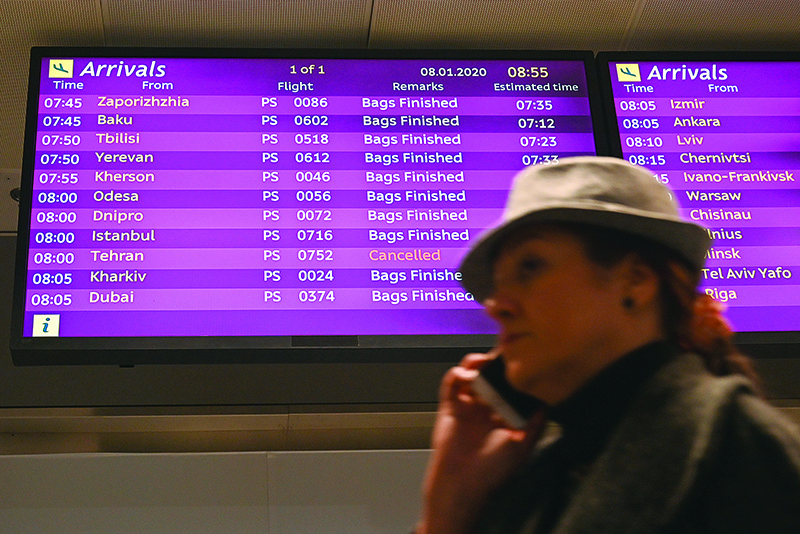 A woman uses a smartphone as she walks past an arrivals board displaying the Ukraine International Airlines Flight PS752 from Tehran marked as cancelled at the Boryspil airport outside Kiev on January 8, 2020. - All passengers and crew on board the Ukrainian Boeing 737 plane that crashed shortly after take-off from Tehran on January 8, 2020 were killed, Ukrainian President Volodymyr Zelensky said. (Photo by Sergei Supinsky / AFP)