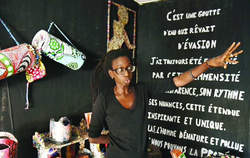 Artist Haby Diallo gestures next to her work during the Tambambalou exhibition in the Madina District of Dakar, on December 12, 2019. - The neighbourhood has its roots in Senegal's colonial past, when in 1914 French authorities moved black people from central Dakar's Plateau neighbourhood, according to Ibrahima Thioub. Since then, the tight-knit community has nurtured artists across generations and has retained its identity even as new migrants moved in from the countryside. (Photo by SEYLLOU / AFP)