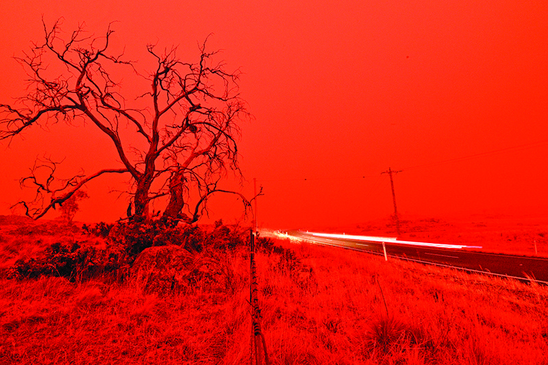A long exposure picture shows a car commuting on a road as the sky turns red from smoke of the Snowy Valley bushfire on the outskirts of Cooma on January 4, 2020. - Up to 3,000 military reservists were called up to tackle Australia's relentless bushfire crisis on January 4, as tens of thousands of residents fled their homes amid catastrophic conditions. (Photo by SAEED KHAN / AFP)