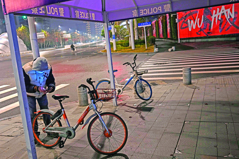 A man wearing a protective facemask tries to take a bicycle on a street in Wuhan on January 26, 2020, a city at the epicentre of a viral outbreak that has killed at least 56 people and infected nearly 2,000. - China on January 26 expanded drastic travel restrictions to contain an epidemic that has killed 56 people and infected nearly 2,000, as the United States, France and Japan prepared to evacuate their citizens from a quarantined city at the outbreak's epicentre. (Photo by Hector RETAMAL / AFP)