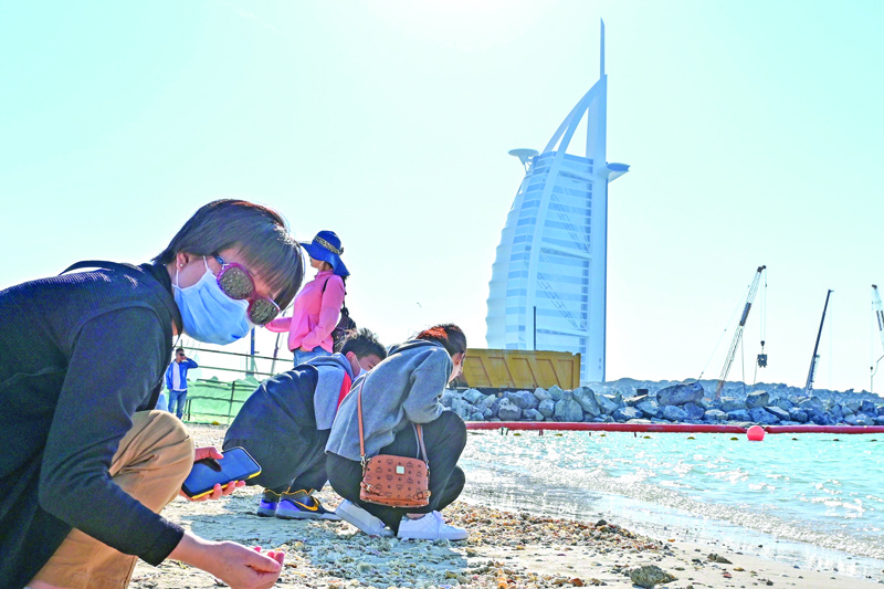 Tourists wearing surgical masks search for seashells on a beach next to Burj Al Arab on January 29 2020. - The United Arab Emirates announced the first confirmed cases of the new coronavirus in the Middle East, with a four-member Chinese family from Wuhan found to be infected. (Photo by GIUSEPPE CACACE / AFP)