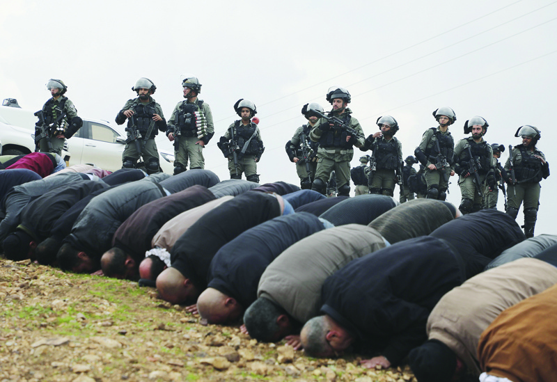 Palestinian demonstrators pray next to Israeli soldiers standing guard during a protest outside the West Bank village of Tubas, near the Jordan Valley, on January 29, 2020, against the US President Donald Trump's peace proposals. - President Donald Trump's long delayed Middle East peace plan won support in Israel but was bitterly rejected by Palestinians facing possible Israeli annexation of key parts of the West Bank. (Photo by JAAFAR ASHTIYEH / AFP)