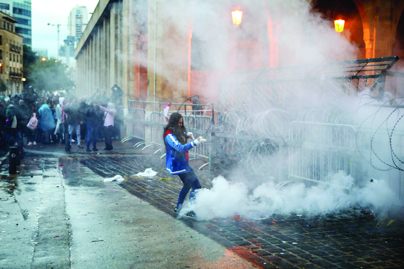 TOPSHOT - A Lebanese anti-government protester kicks back a tear gas canister fired by riot police from behind the barricaded road leading to parliament in central Beirut on January 19, 2020. - Dozens of stone-throwing demonstrators defied police water canons in the Lebanese capital, a day after rare violence between both sides injured more than 400 people. (Photo by PATRICK BAZ / AFP)