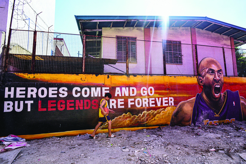 TOPSHOT - A boy with a basketball walks past a wall painted for former Los Angeles Lakers basketball player Kobe Bryant, following his death overnight in the US, in Manila on January 27, 2020. (Photo by Maria TAN / AFP)
