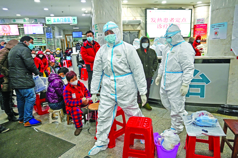 Medical staff members wearing protective clothing to help stop the spread of a deadly virus which began in the city, walk next to patients (L) waiting for medical attention at the Wuhan Red Cross Hospital in Wuhan on January 25, 2020. - The Chinese army deployed medical specialists on January 25 to the epicentre of a spiralling viral outbreak that has killed 41 people and spread around the world, as millions spent their normally festive Lunar New Year holiday under lockdown. (Photo by Hector RETAMAL / AFP)