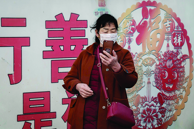 BEIJING: A woman wearing a protective mask to help stop the spread of a deadly virus checks her look with the camera of her smartphone at Beijing railway station yesterday. - AFP