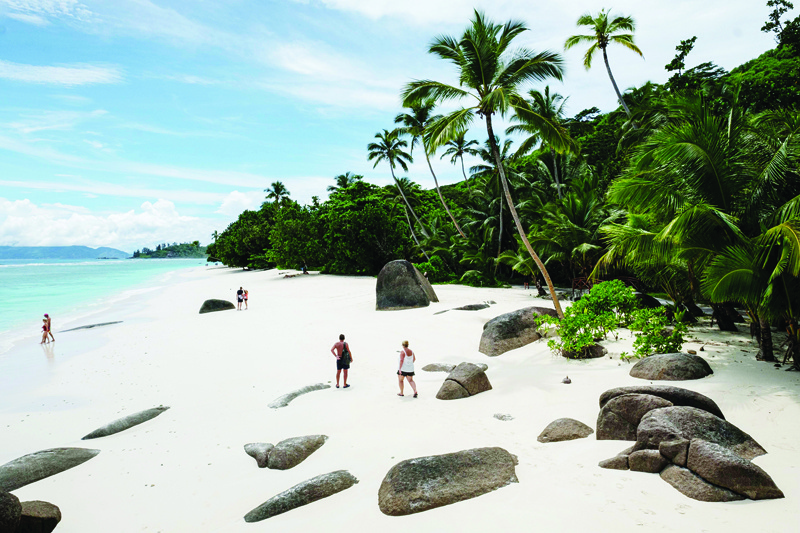A picture taken on November 16, 2019, shows tourists  walking on the beach with granite rocks on in Silhouette Island, the third largest island, Seychelles. - The Seychelles, a byword for luxury holidays and Instagram-perfect beaches, lives off tourism. But the idyllic honeymoon abode is confronting a tug-of-war over how to keep the economy growing, while protecting its fragile ecosystem.nHigh-end tourism, mainly from Europe, helped pull the Seychelles from the brink of financial ruin after the 2008 economic crisis. Visitor numbers doubled in the decade that followed to around 360,000 today. (Photo by Yasuyoshi CHIBA / AFP)