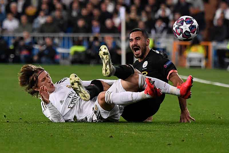Real Madrid's Croatian midfielder Luka Modric (L) falls with Manchester City's German midfielder Ilkay Gundogan during the UEFA Champions League round of 16 first-leg football match between Real Madrid CF and Manchester City at the Santiago Bernabeu stadium in Madrid on February 26, 2020. (Photo by PIERRE-PHILIPPE MARCOU / AFP)
