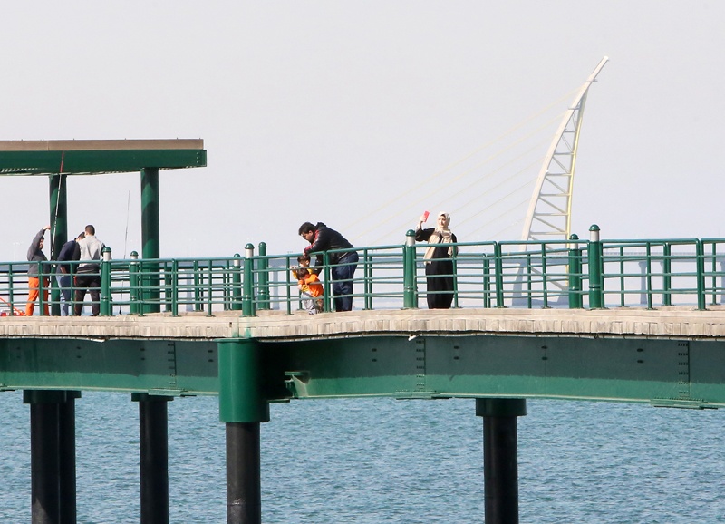 A woman (R) takes a selfie as the Jaber Causeway is seen in the background while standing on a fishing pier in Kuwait City on February 2, 2020.