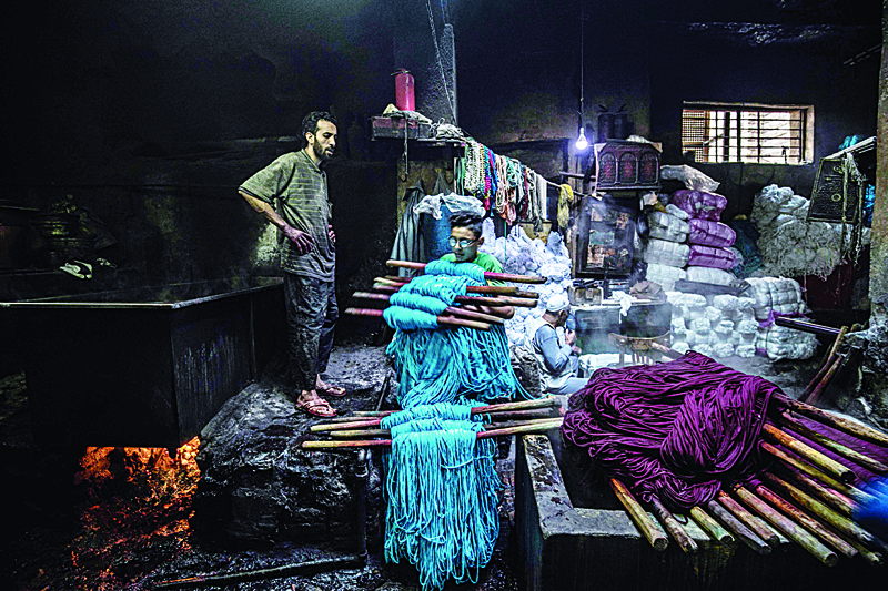 TOPSHOT - A workers carries away dyed yarns at a traditional hand-dying workshop in the Egyptian capital Cairo's centuries old district of Darb al-Ahmar on January 21, 2020. - In Cairo's centuries-old Darb al-Ahmar district, Salama Mahmoud Salama's dye workshop is a multi-coloured den of textiles and busy workers colouring all kinds of fabrics. Salama and his relatives lay out the long, flowing threads, which will be used for everything from handmade shoes to rugs and drapes, and dip them in huge, piping-hot colour baths -- no gloves or masks protecting them from the dyes and chemical fumes. The workshop in Islamic Cairo has been going strong for over a hundred years. (Photo by Khaled DESOUKI / AFP)