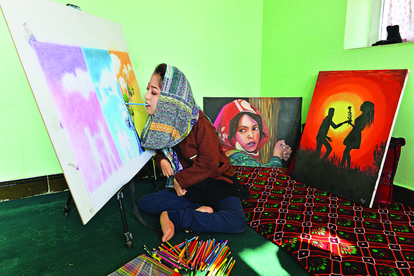 This photo taken on December 5, 2019 shows 19-year-old Afghan artist Robaba Mohammadi painting in her studio in Kabul. - Unable to use her hands, arms, or legs, Afghan artist Robaba Mohammadi has defied unlikely odds in a country that routinely discriminates against women and disabled people. Denied access to school, as a child she taught herself to paint by holding a brush in her mouth, clenching it between her teeth to create elaborate and colourful portraits. (Photo by NOORULLAH SHIRZADA / AFP) / TO GO WITH Afghanistan-disabilities-woman-social,FOCUS by Mushtaq MOJADDIDI