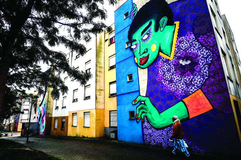 A resident of Quinta do Mocho neighbourhood walk past a mural by French artist Stew, in Sacavem, outskirts of Lisbon, on November 11, 2019. - The image of a black woman removing her white-woman mask is one of the hundreds of murals that cover the buildings of the underprivileged district of Quinta de Mocho in Lisbon, that has been transformeded by street art. (Photo by PATRICIA DE MELO MOREIRA / AFP) / RESTRICTED TO EDITORIAL USE - MANDATORY MENTION OF THE ARTIST UPON PUBLICATION - TO ILLUSTRATE THE EVENT AS SPECIFIED IN THE CAPTION