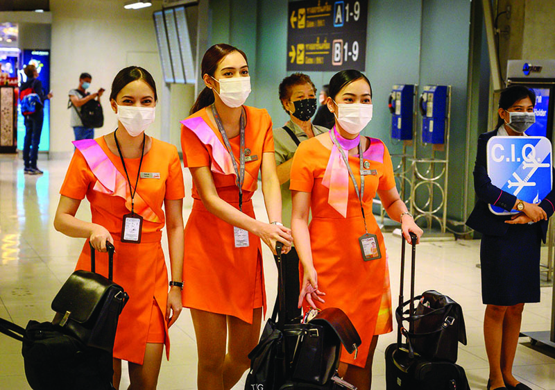 Thai Smile cabin crew members wearing protective facemasks walk next to an airport official (R) waiting for CIQ (China Inspection and Quarantine) passengers at Suvarnabhumi International Airport in Bangkok on February 9, 2020. - The new coronavirus that emerged in central China at the end of last year has killed more than 800 people and spread around the world. (Photo by Mladen ANTONOV / AFP)
