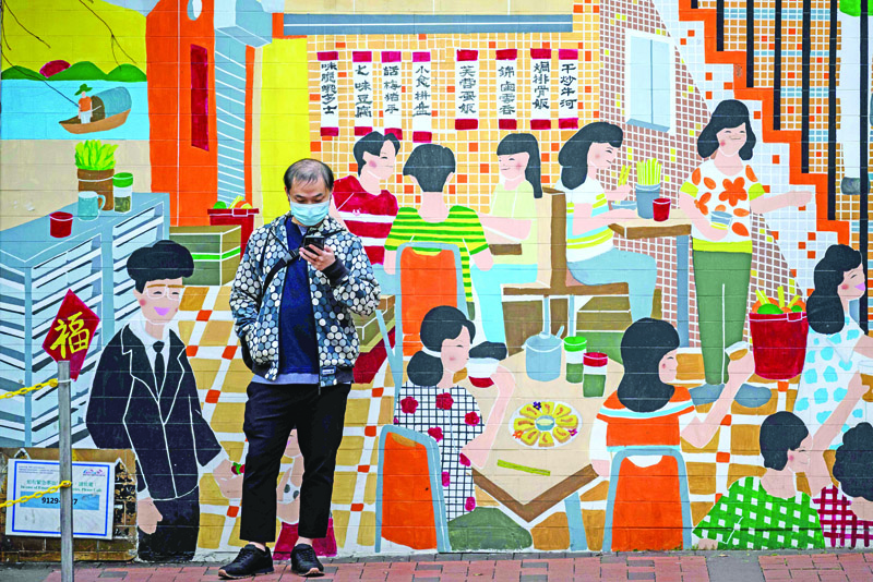 A man wearing a facemask while using his phone stands in front of a mural in Hong Kong on February 4, 2020, as a preventative measure following a virus outbreak which began in the Chinese city of Wuhan. - Hong Kong on February 4 became the second place outside mainland China to report the death of a coronavirus patient as officials said they feared local transmissions were increasing in the densely populated city. (Photo by Anthony WALLACE / AFP)