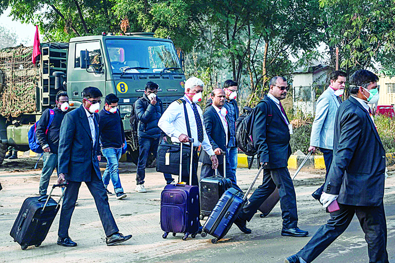 Crew members and officials wearing protective facemasks carry their belongings at Indira Gandhi International Airport following the evacuation of Indian nationals evacuation from the Chinese city of Wuhan, in New Delhi on February 1, 2020. - A virus similar to the SARS pathogen has killed 259 people in China and spread around the world since emerging in a market in the central Chinese city of Wuhan. (Photo by Money SHARMA / AFP)