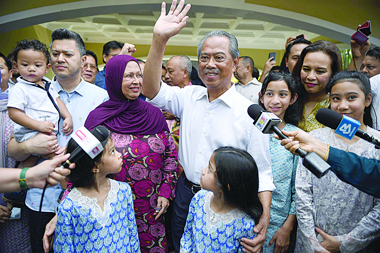 Malaysia's former interior minister Muhyiddin Yassin (C) and his family wave to the press shows outside his home in Kuala Lumpur on February 29, 2020. - Muhyiddin was named as Malaysia's new prime minister on February 29, royal officials said, signalling the end of Mahathir Mohamad's rule and return to power of a scandal-plagued party. (Photo by Mohd RASFAN / AFP)