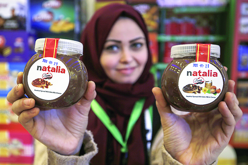 A shop employee holds up jars of a Gazan version of a world famous spread, dubbed 'Natalia', in Gaza city on February 12, 2020. - Al-Arees's products are Gazan but their components are not, as few of the basic raw ingredients are produced in the impoverished Mediterranean coastal strip. nIsrael controls all goods that enter Gaza, imposing a blockade that tightened after the tiny enclave was seized by the Islamist group Hamas in 2007. (Photo by MOHAMMED ABED / AFP)
