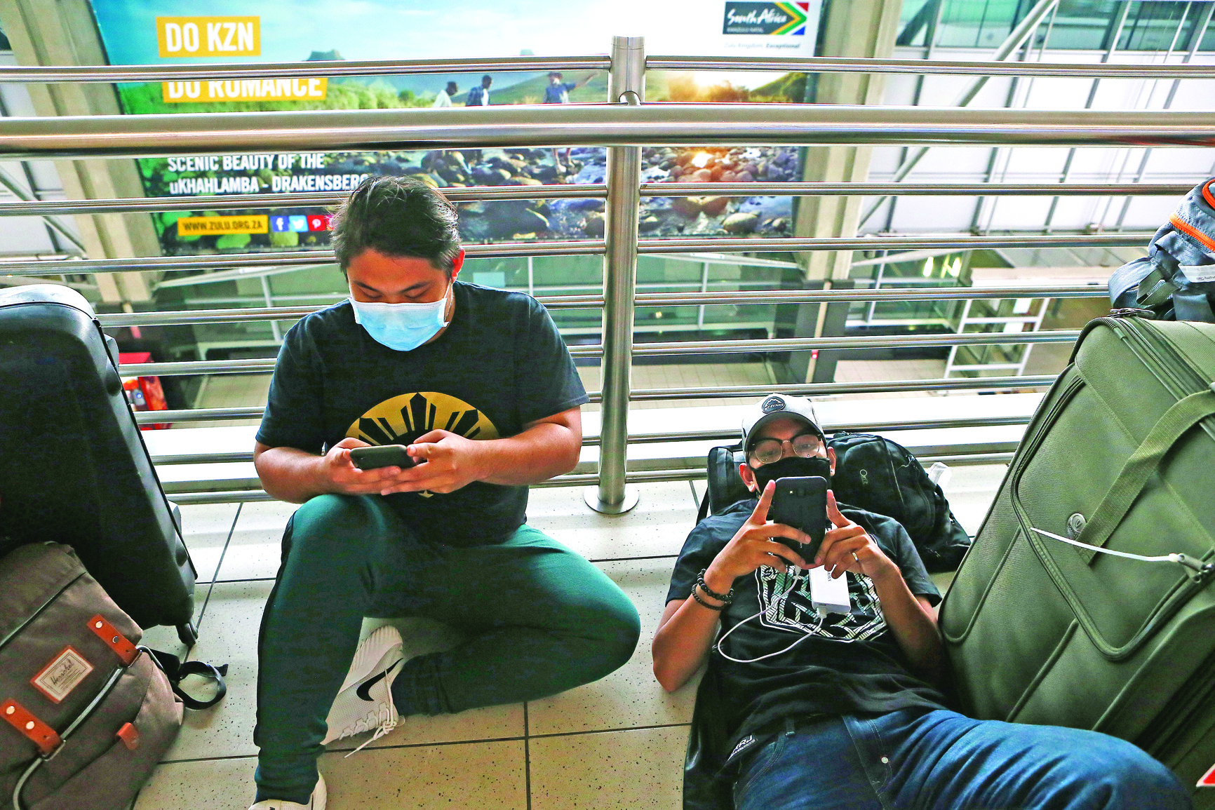 Travellers wearing masks use their mobile phones at OR Tambo International Airport, Johannesburg, on February 28, 2020 amid fear of Covid-19 epidemic. (Photo by Phill Magakoe / AFP)