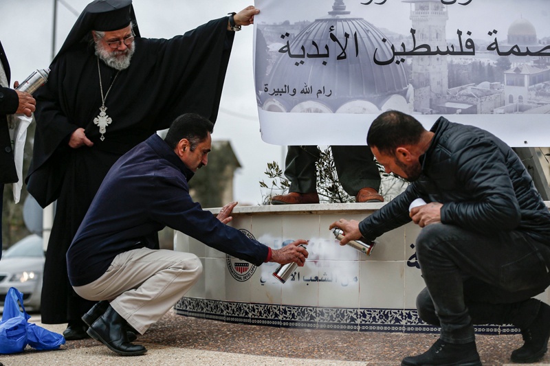 Archimandrite Abdullah Yulio (top), parish priest of the Melkite Greek Catholic church in Ramallah, watches as Palestinian protesters spray paint to cover the logo of the United States Agency for International Development (USAID), while protesting against US President Donald Trump's Middle East peace plan, in the city of Ramallah in the occupied West Bank on February 4, 2020. (Photo by ABBAS MOMANI / AFP)
