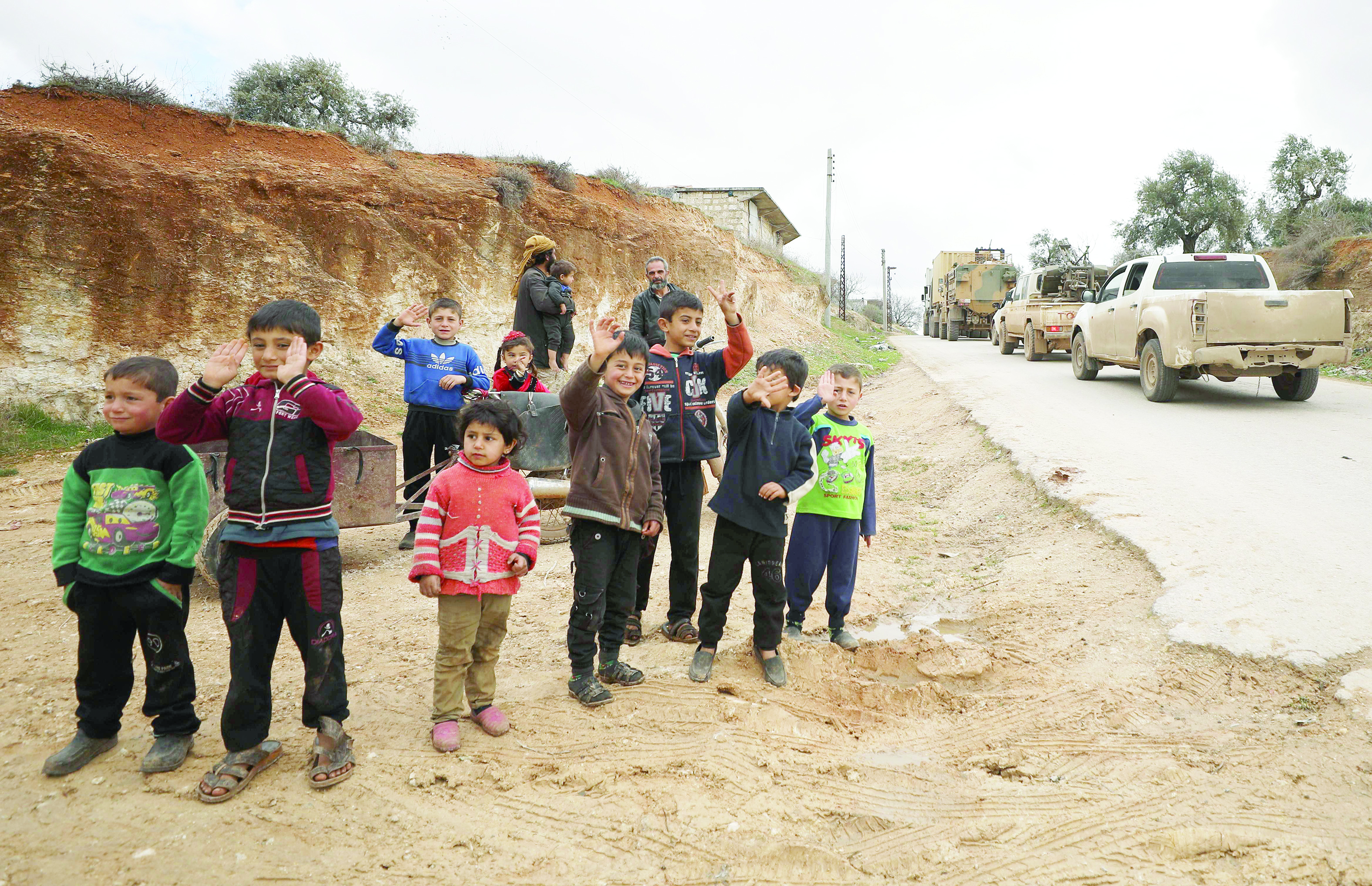 Children watch as a Turkish military convoy that crossed into the Syrian territory via the Kafr Lusin border, passes near Syria's northwestern city of Idlib as it heads toward the south of the Idlib province, on February 22, 2020. (Photo by Omar HAJ KADOUR / AFP)