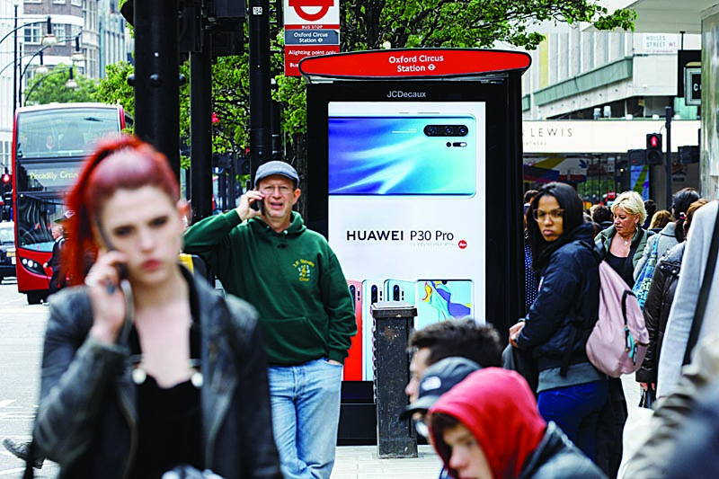 (FILES) In this file photo taken on April 29, 2019, pedestrians use their mobile phones near a Huawei advert at a bus stop in central London. - Britain is hoping to negotiate a comprehensive free-trade agreement with the United States after Brexit, but a number of thorny issues stand in the way. (Photo by Tolga Akmen / AFP)