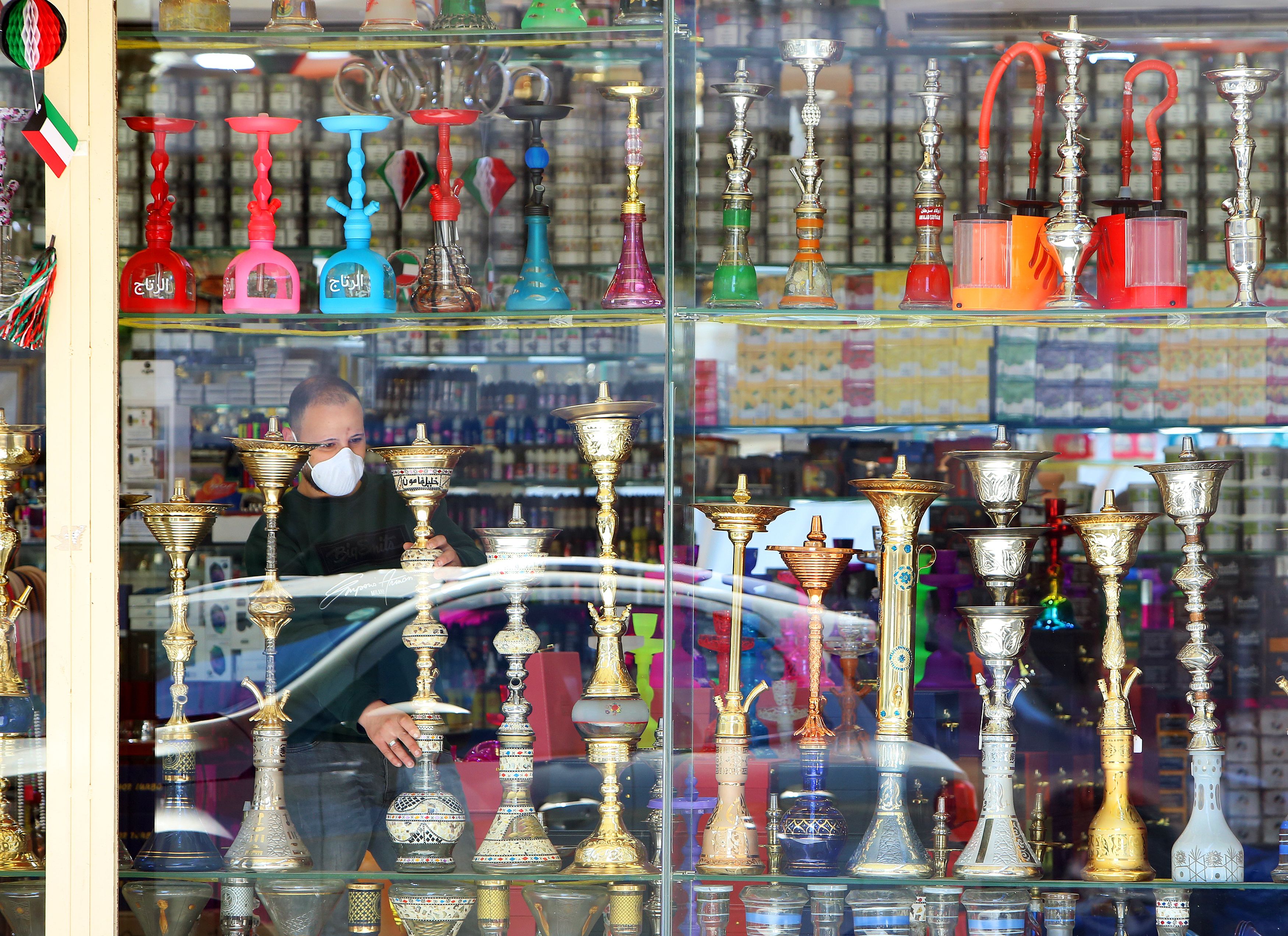 A cigarette and hookah seller wearing a protective mask looks through the front of his store in Kuwait City on March 5, 2020. The State of Kuwait issued a decision to ban hookah in public cafes until further notice in order to prevent the spread of the Corona virus.