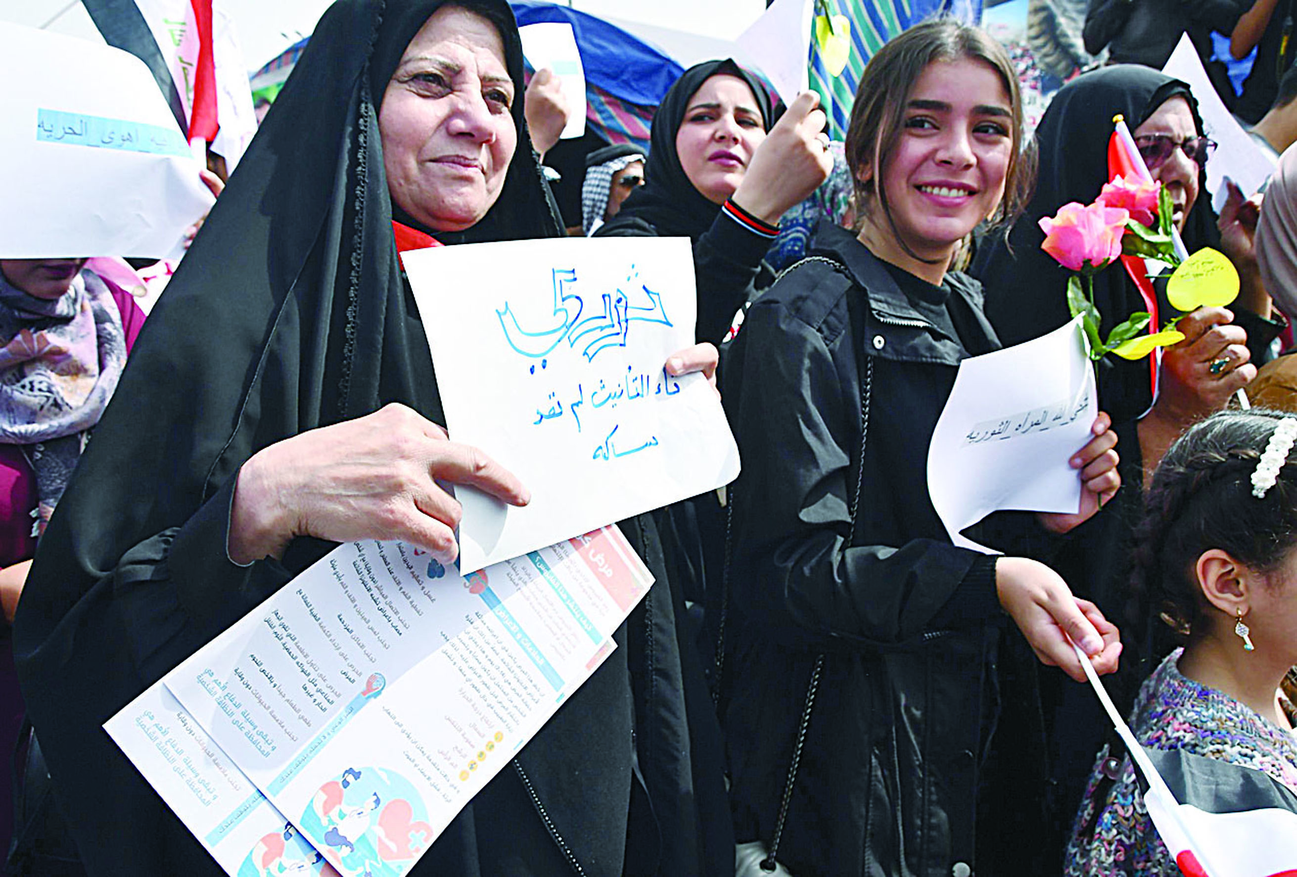 Iraqi women holding a placarda and roses take part in an anti-government demonstration in Iraq's southern city of Nasiriyah in Dhi Qar province, during the international Women's Day on March 8, 2020. (Photo by Asaad NIAZI / AFP)