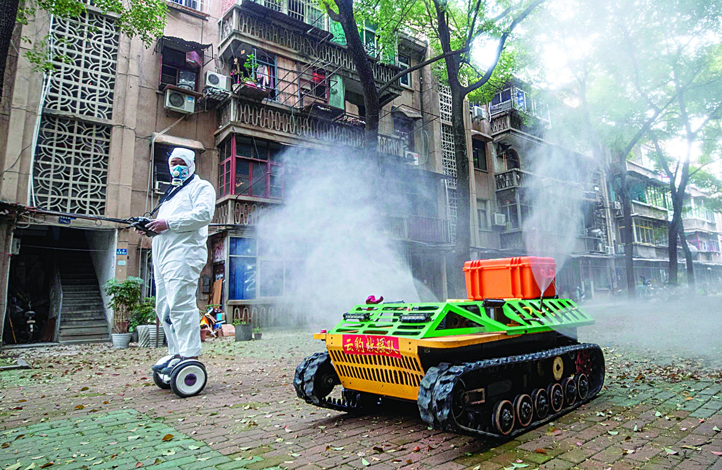TOPSHOT - A volunteer operates a remote controlled disinfection robot to disinfect a residental area amid the COVID-19 coronavirus outbreak in Wuhan in China's central Hubei province on March 16, 2020. - China tightened quarantine measures for international arrivals on March 16 as the country worries about a rise in imported cases of the deadly coronavirus and anger rages online at how Europe and the United States are handling the pandemic. (Photo by STR / AFP) / China OUT