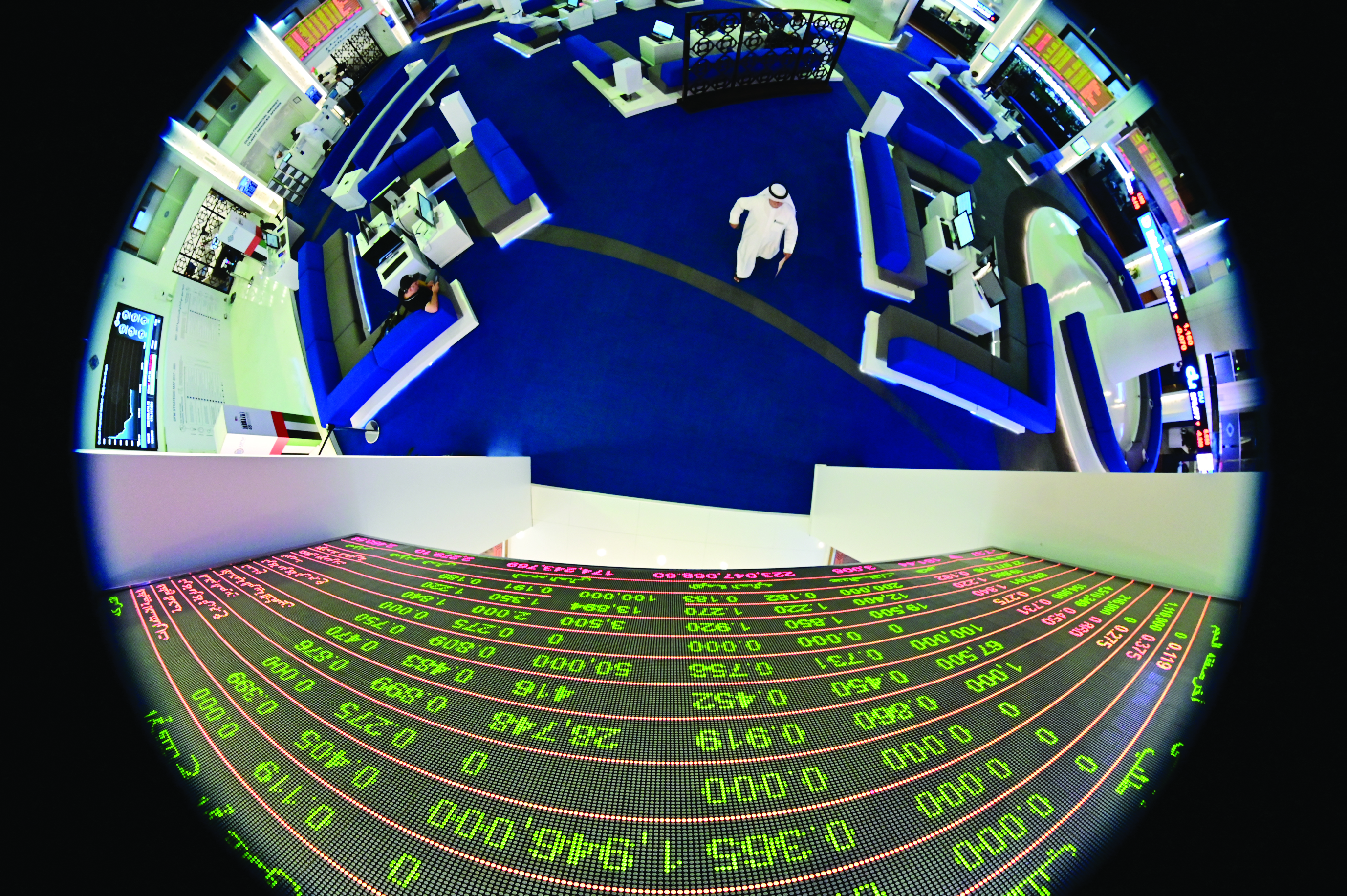 A picture taken with a fisheye lense shows traders walking by beneath a stock display board at the Dubai Stock Exchange in the United Arab Emirates, on March 8, 2020. - Saudi's stock exchange fell 6.5 percent and other Gulf markets tumbled to multi-year lows at the start of trading after OPEC and its allies failed to clinch a deal over oil production cuts. (Photo by GIUSEPPE CACACE / AFP)