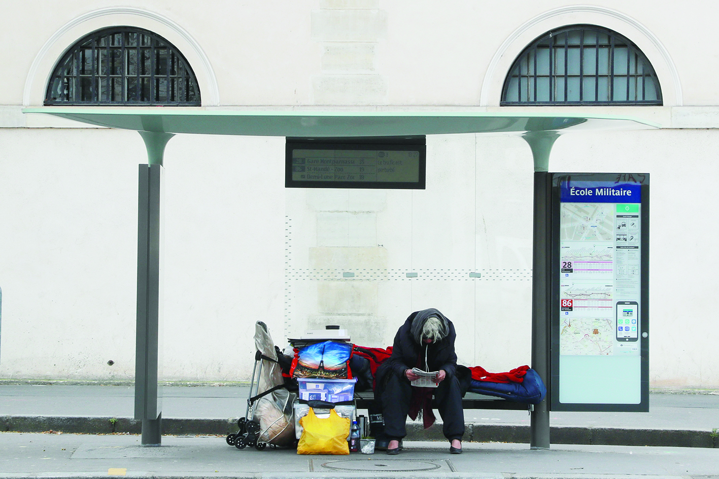 A homeless sits at a bus stop on march 22, 2020, in Paris, as a strict lockdown comes into effect to stop spread of the COVID-19 caused by novel coronavirus in the country prohibiting all but essential outings in a bid to curb coronavirus spread. (Photo by Ludovic MARIN / AFP)