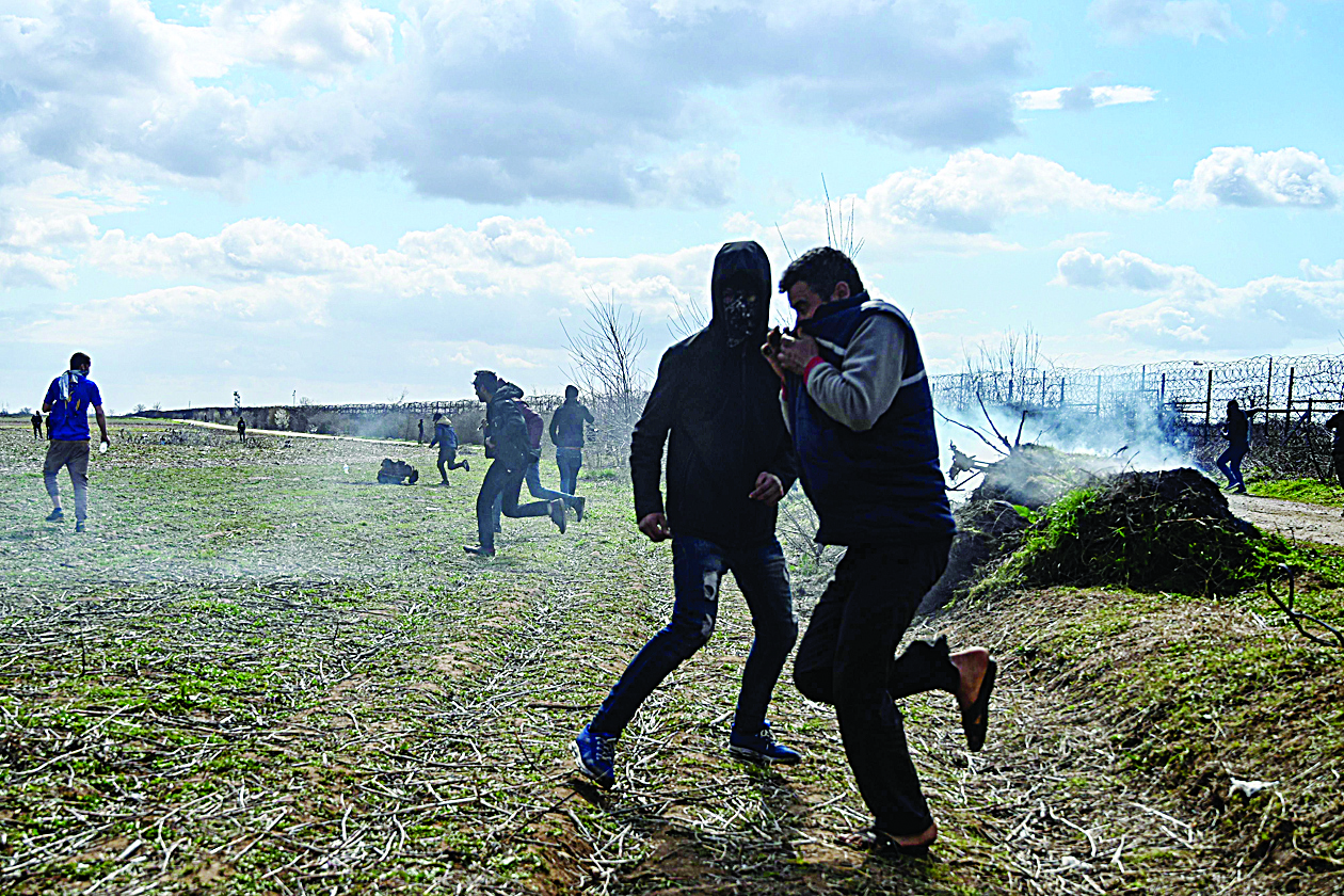 Migrants run away from tear gas at the Turkey-Greece border buffer zone near Pazarkule crossing gate in Edirne, on March 7, 2020, during clashes between Greek police and migrants trying to cross to the Greek side. - Greece plans to build two new temporary camps to house hundreds of additional asylum seekers who arrived after a surge enabled by Turkey, the migration minister said Saturday. (Photo by Ozan KOSE / AFP)