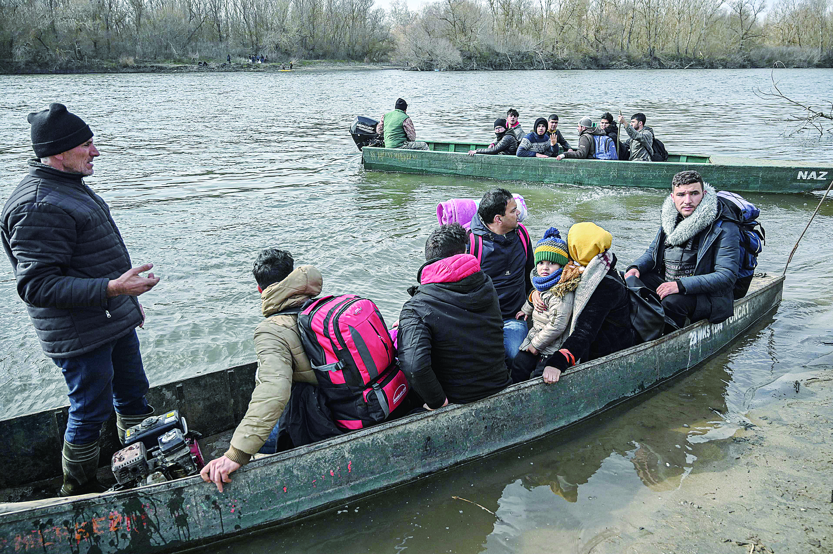Migrants take boats near Edirne while other migrants wait at Greece side, as they attempt to enter Greece by crossing the Maritsa river, on March 1, 2020. - Thousands more migrants reached the Turkish border with Greece on March 1, 2020, AFP journalists said, after President threatened to let them cross into Europe. At least 2,000 people including women and children arrived on the morning from Istanbul and walked through a field towards the Pazarkule border gate, a correspondent said. The group included Afghans, Syrians and Iraqis. (Photo by Ozan KOSE / AFP)