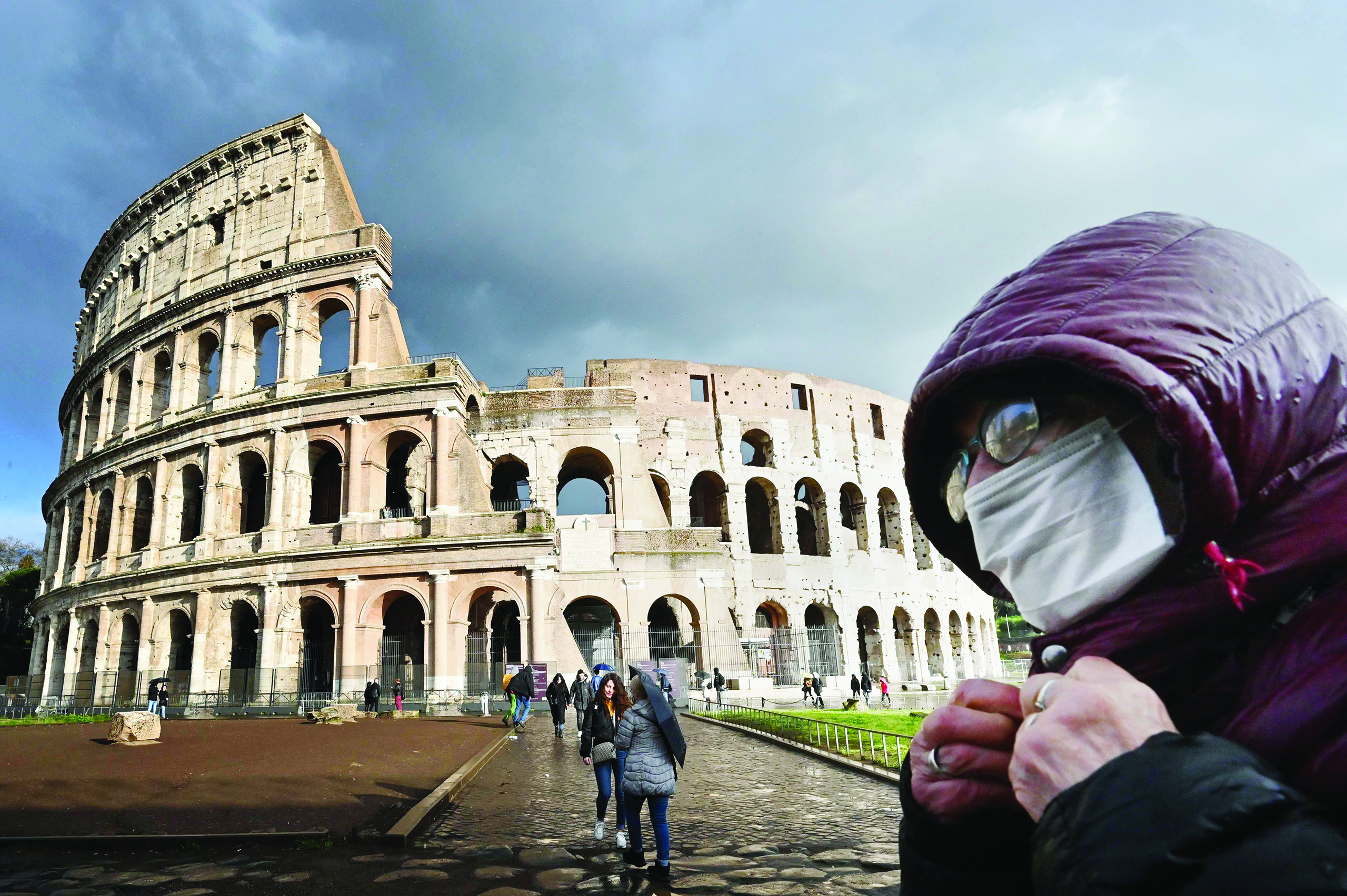TOPSHOT - A man wearing a protective mask passes by the Coliseum in Rome on March 7, 2020 amid fear of Covid-19 epidemic. - Italy on March 6, 2020 reported 49 more deaths from the new coronavirus, the highest single-day toll to date, bringing the total number of fatalities over the past two weeks to 197. (Photo by Alberto PIZZOLI / AFP)