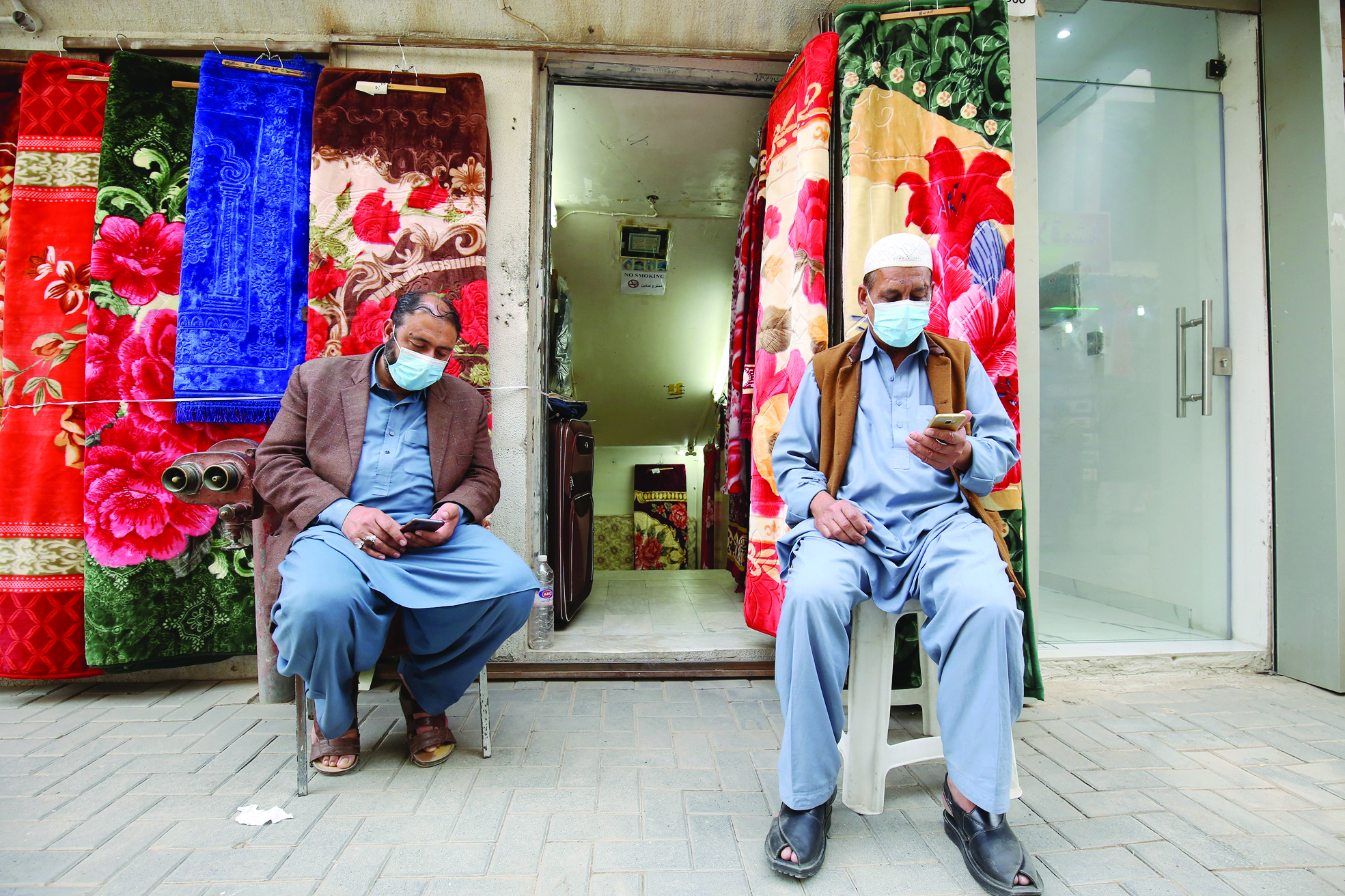 Vendors, wearing protective masks, sit outside their shop in Kuwait City on February 26, 2020. - The new coronavirus hit four more Middle Eastern states, with Bahrain, Iraq, Kuwait and Oman reporting new cases and the UAE calling on its citizens not to travel to Iran and Thailand. Kuwait, for its part, called off celebrations for the Gulf state's national day, as it confirmed its first three cases of the virus, all connected to Iran. (Photo by YASSER AL-ZAYYAT / AFP)