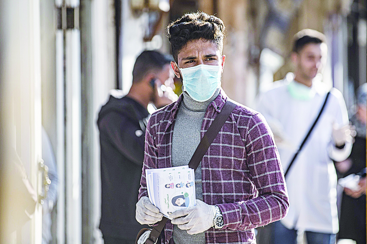A health volunteer wearing a protective mask, due to fears of COVID-19 coronavirus spread, hands out pamphlets warning people about the disease along a market street in Qamishli in Syria's northeastern Hasakah province on March 22, 2020. - Deprived of cross-border aid and already low on medical supplies, northeast Syria is grappling with the threat of a virus outbreak that aid groups and officials fear could ravage the region. Home to sprawling displacement camps hosting some 100,000 people, including the families of the Islamic State group, the Kurdish-held northeast has yet to declare a single infection. But with the region severely under-equipped, local officials have started to sound the alarm after Damascus announced the country's first coronavirus case on Sunday. (Photo by DELIL SOULEIMAN / AFP)