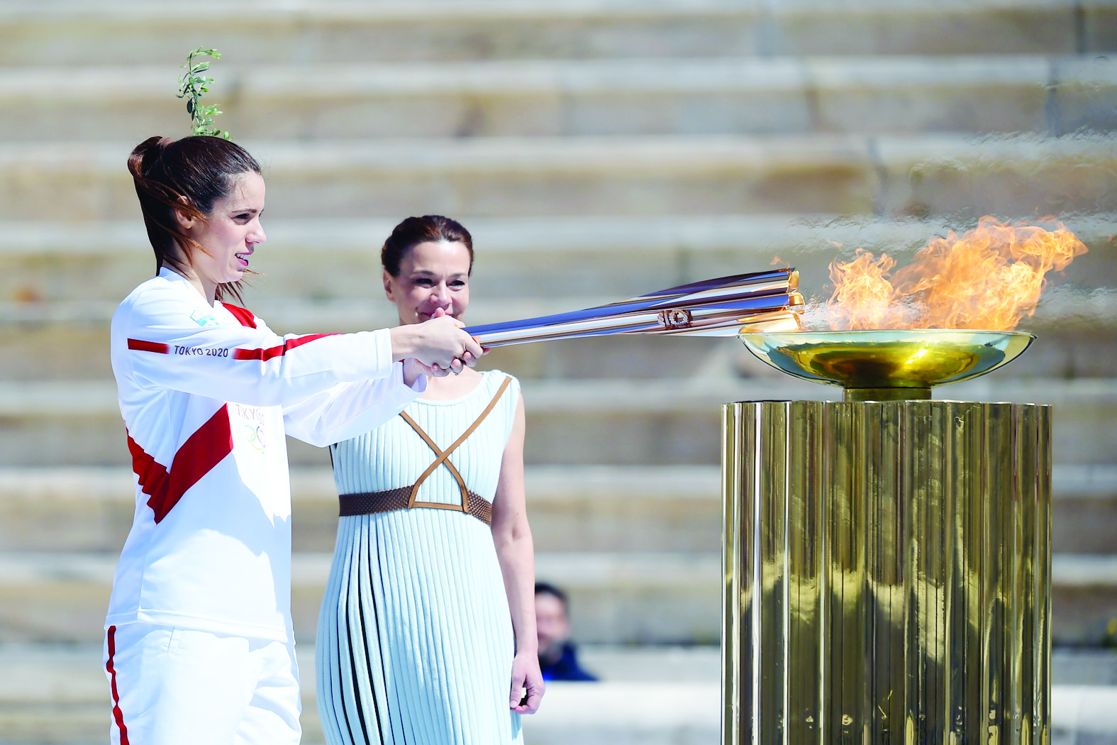 An athlete lights the Olympic torch during the olympic flame handover ceremony for the 2020 Tokyo Summer Olympics, on March 19, 2020 in Athens. (Photo by ARIS MESSINIS / various sources / AFP)