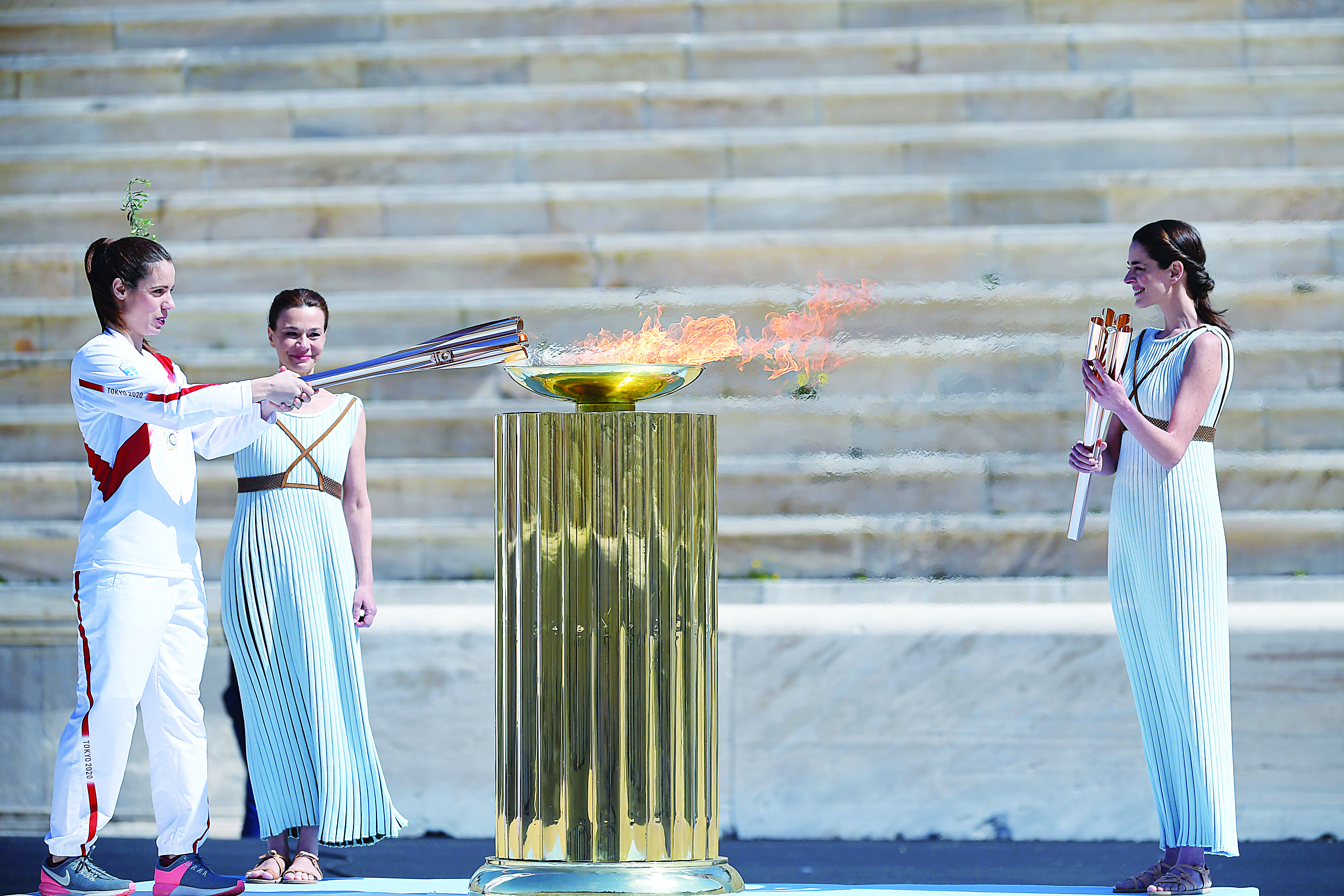 An athlete lights the Olympic torch during the olympic flame handover ceremony for the 2020 Tokyo Summer Olympics, on March 19, 2020 in Athens. (Photo by ARIS MESSINIS / various sources / AFP)