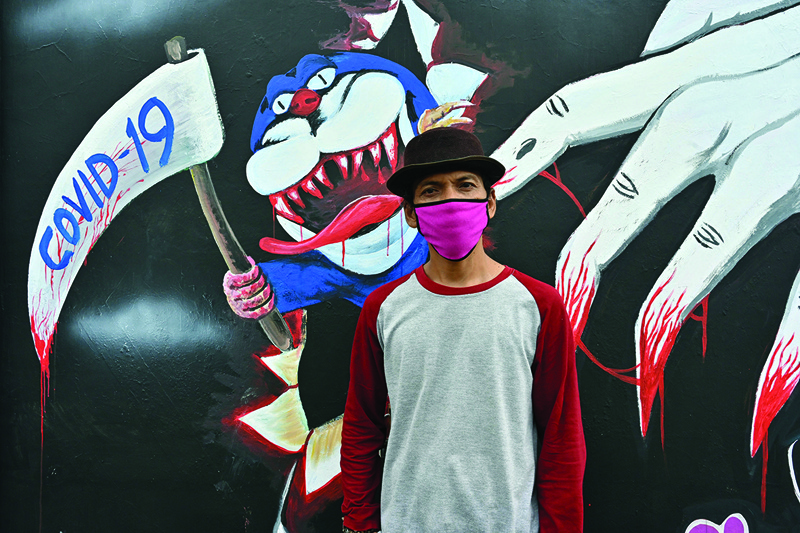 This picture taken on April 9, 2020 shows mural artist Sulis Listanto posing next to his artwork as local artists join the campaign in the fight against the COVID-19 coronavirus outbreak in Depok, West Java. - From scythe-wielding monsters to a globe fending off the COVID-19 coronavirus with an umbrella, a group of Indonesian artists has turned to wall murals to help clamp down on a surging tide of infections. (Photo by ADEK BERRY / AFP) / RESTRICTED TO EDITORIAL USE - MANDATORY MENTION OF THE ARTIST UPON PUBLICATION - TO ILLUSTRATE THE EVENT AS SPECIFIED IN THE CAPTION