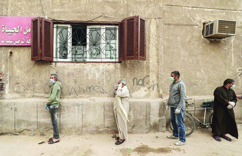 Egyptian men wearing masks wait outside a centre of non-governmental organisation Egyptian Food Bank to receive cartons with foodstuffs on April 05, 2020, as the charity distributes aid to people who lost their jobs due to the coronavirus pandemic crisis, in the Egyptian capital Cairo. - The large Cairo-based charity organisation EFB has been at the forefront of a public relief effort in the most populous Arab country, where one third of the population of over 100 million lives in poverty, surviving on about $1.50 or less a day. virus. Egypt so far has recorded 85 deaths out of 1,322 confirmed cases of the COVID-19 illness. (Photo by Mohamed el-Shahed / AFP)