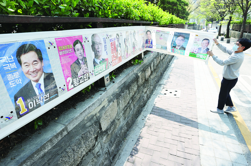 A South Korean official removes a poster of multiple candidates running in the parliamentary elections after the polls in Seoul on April 16, 2020. - South Korea's left-leaning ruling party has won a landslide election victory, partial results showed on April 16, after the coronavirus pandemic turned the political tide in President Moon Jae-in's favour. (Photo by - / YONHAP / AFP) / - South Korea OUT / REPUBLIC OF KOREA OUT  NO ARCHIVES  RESTRICTED TO SUBSCRIPTION USE