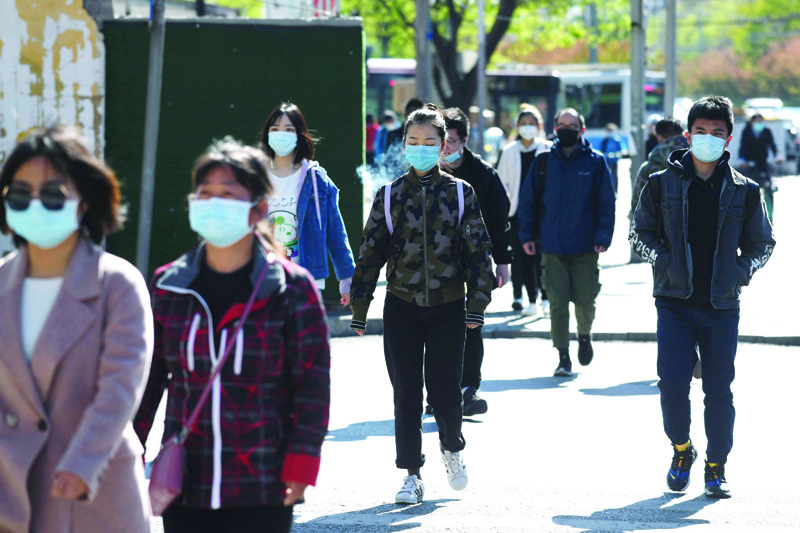 People wear face masks amid concerns of the COVID-19 coronavirus as they walk to a subway station in Beijing on April 23, 2020. (Photo by GREG BAKER / AFP)